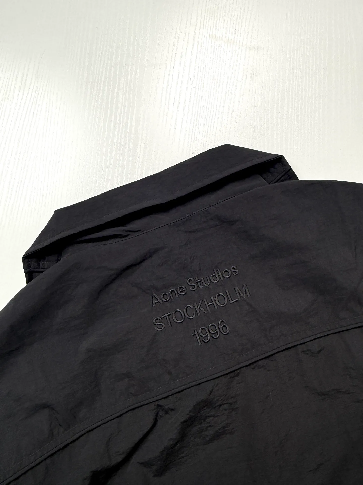 Acne Studio short embroidered functional wind jacket is made of original custom-woven micro-wrinkle nylon fabric. The color of the fabric is consistent with the original version, without a stiff plastic feel. The stand-up collar has a full zipper structure, double zippered hidden pockets on the front, and all zipper accessories are the same as the original ones; the raglan sleeves are cut, the short drop-waist style is designed, and the length, shoulder width, hem drawstring, and cuff elastic cuffs are all made according to the original pattern. version, the back is embroidered with dark patterns of the same color, and the font spacing, stitch density, and embroidery depth are strictly aligned, with a low-key tone-on-tone effect that is not obtrusive; the full set of accessories for the collar tag and tag are restored, and the thread routing and segmentation cutting processes are reproduced 1:1. Size: 32/34/36